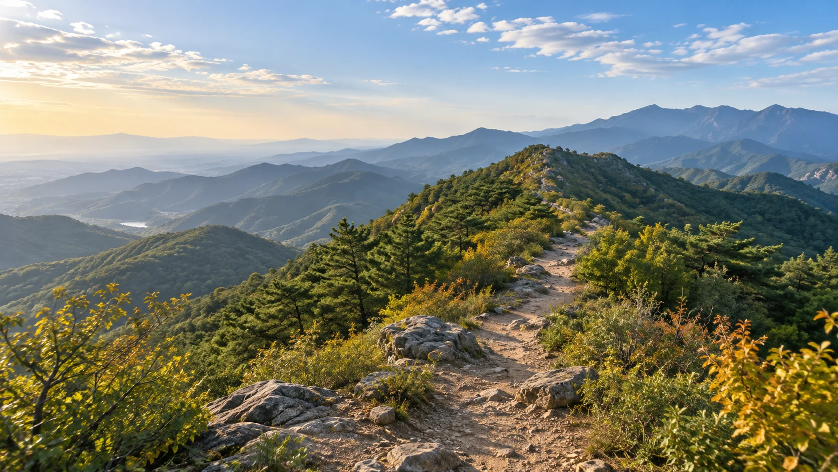 北京西山十月初山地，仍以绿色为主的松柏和阔叶林，局部浅金初秋叶片，一条中央土石小径沿低矮山脊前进，远处连绵灰蓝山丘，光线温暖通透，不画满山通红或长城